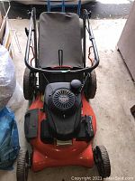 Overhead front view of orange mower deck, black Honda engine cover, foldable handle and grey fabric bag