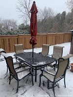 Full view of rectangular table, six sling chairs and closed red umbrella on snow-covered patio