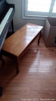Wood piano bench shown next to a piano and window, highlighting height and overall shape.