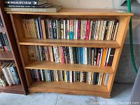 Wooden shelving unit with multiple shelves filled with assorted hardcover and paperback books.