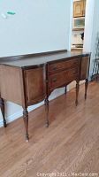 Front view of the vintage wooden sideboard showing two drawers and curved doors on either side and turned legs.