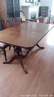 Full angle showing wooden table top and one pedestal base with metal claw feet on hardwood floor in well-lit room.