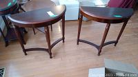 Two matching Bombay wood demilune tables with semicircular dark brown wood tops, turned legs, and curved stretcher supports on a wood floor.