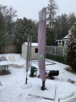 Closed purple-covered parasol standing next to folded rotary clothesline in snowy backyard