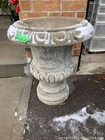 Concrete urn with carved decorative patterns, placed outdoors with snow on ground
