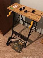 Photo of Ultra Steel adjustable work bench showing wooden top with holes and yellow cranks, black metal legs, and drill bit set on the floor