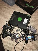Top view of original Xbox console with five tangled wired controllers on carpet