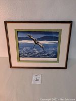 Framed print depicting a pelican in flight over water with mountains and sky.
