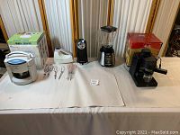Wide view of all five kitchen appliances on table showing jar opener, mixer with beaters, blender, can opener, and cappuccino maker.