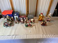 Overall shot of seven porcelain holiday figurines including one light-up schoolhouse and several Santa Claus themed pieces.