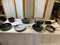 Overview of all cookware on table including cast iron Dutch ovens with lids, a cast iron pot, round and square pans from Cephalon and other brands.