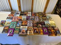 Photo showing an array of 40 paperback and hardcover books spread across a table, genres include fantasy and mystery with various cover arts.