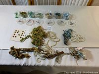 Overview of collection with loose beads in containers, decorative trims, pearl strands, and pins spread out on a table.