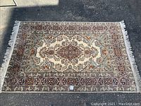 Full view of the rectangular hand knotted wool pile rug laid flat on pavement, showing central medallion pattern and fringed edges.