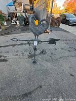 Full view of metal rooster weather vane, arrow and directional letters on asphalt background