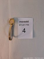 Full view of Seiko gold tone Mickey Mouse watch with expandable band next to a MaxSold note.