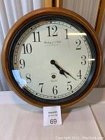 Full view of the round wall clock showing wooden frame, white face, black numbers, and hands with some glare.