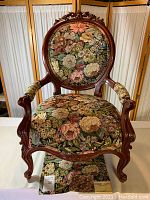 Front view of carved wooden armchair with floral tapestry upholstery