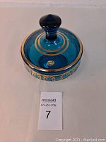 Top-down view showing lid with maker's sticker and gold bands on aqua blue crystal.