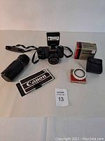 Wide-angle shot showing Canon T50 camera body with attached 50mm lens, zoom lens, flash, two filter boxes, product guide, and camera strap.