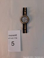 Full view of vintage Ferrari wristwatch with black and gold-tone metal band lying flat on a white surface with lot card.