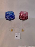 Two hand cut lead crystal wine glasses, cobalt blue and cranberry, shown side by side on table surface.