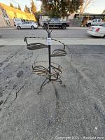 Full view of black wrought iron plant stand showing four circular ledges and overall structure on outdoor pavement.