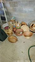 Grouped assortment of baskets and vases against a cinderblock wall, showing variety of sizes and shapes.