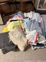 Mixed bedding stack including a beige knitted wool blanket with fringe, sheets and embroidered pillowcases in floral designs and different colors.