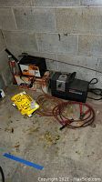 Photo of Craftsman air compressor, Atec battery charger, license plates, and hose on concrete floor