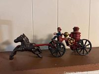 Side view of cast metal horse drawn fire engine showing front horses and firefighter figure on red engine with black wheels.