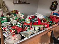 Full view of various Christmas holiday items including figurines, plates, giftwrap, and decorations spread on a surface