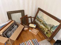 Photo showing the large framed landscape print leaning against the wall along with several wooden plaques and frames on the floor and in a box.
