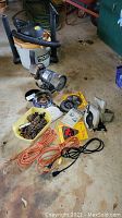 Overall lot showing Ridgid shop vac, bench grinder, circular saw, saw blades, extension cords, and accessories on concrete floor
