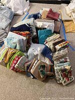 Photo showing a pile of folded assorted kitchen and bath linens including towels and small rugs with multiple colors and patterns.