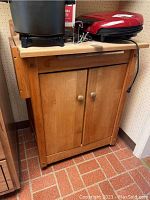 Front view of wooden kitchen cart with flat top surface, two-door cabinet, and items on top.