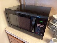 Front and top view of black Magic Chef microwave oven on countertop, showing door, handle, control panel with numeric keypad and digital display.