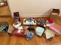 Full view of all items included in the lot. Shows various massagers, exercise accessories, grooming devices, hair tools, and related items arranged on floor.