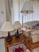 Two matching 66 Pieri Mid-Century Modern lamps with pleated lampshades and wooden bases, positioned on floor next to sofa and wooden lamp table with magazine rack.