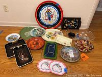 Photo showing entire assortment of trays and bowls on floor, various sizes, materials, and painted designs visible.