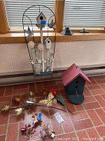 Photo showing signed metal butterfly and leaf sculpture, two birdhouses, and various yard decorations arranged on floor and near window