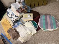 Assorted folded table linens including cloth tablecloths, placemats, runners, and chair cushions arranged on carpeted floor near a couch.