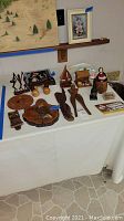 Table top with multiple wooden decorative items including plaques, nutcracker, moose-shaped massager, carved figurines, and a feather art piece of peacocks visible above the table on the shelf.