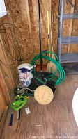 Photo showing garden hose coiled on black hose hanger, outdoor thermometer, shovel, brooms, and bag of rock salt in wooden shed corner.