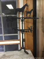 Full front view of cast iron weathervane with horse and foal silhouettes, directional letters on tripod base