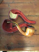 Wooden tobacco pipe with amber stem displayed in open red velvet-lined case on wooden surface