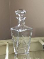 Full view of clear crystal decanter with stopper against neutral background