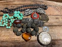 Overview of assorted antique jewelry pieces displayed on a wooden surface showing necklaces, pendants, bracelets, and a pocket watch.