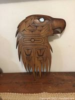 Front view of the carved wooden eagle head plaque with intricate First Nations design and abalone shell inlay for the eye.