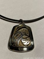 Front view of trapezoidal silver pendant with raised gold whale design